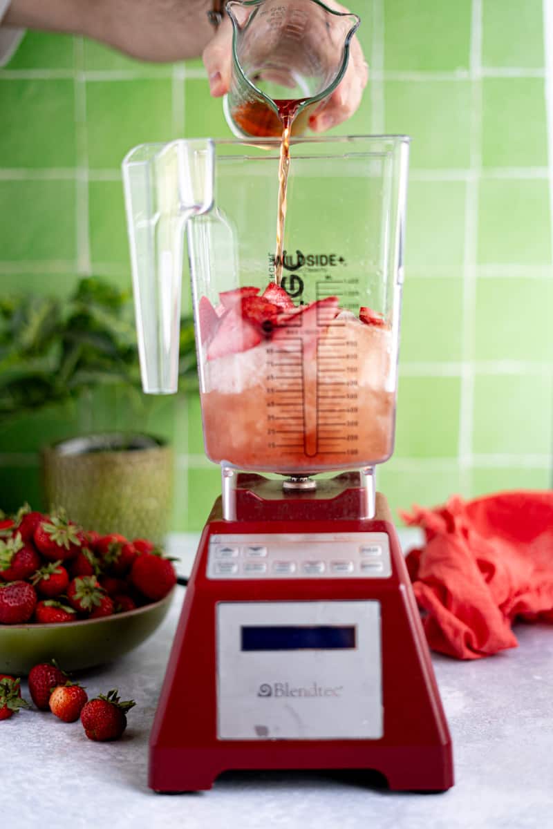 Adding in the strawberry simple syrup to the blender jar to make frozé.