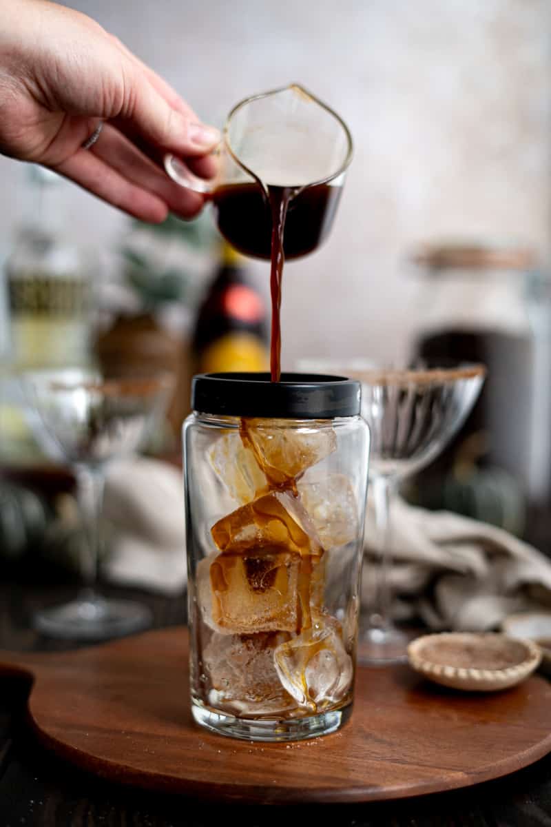 Pouring espresso into a cocktail shaker filled with ice.