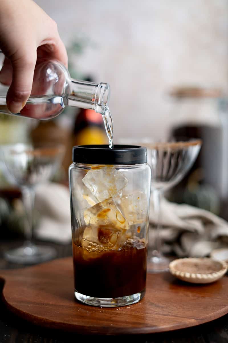 Pouring vodka into a cocktail shaker filled with espresso and ice.