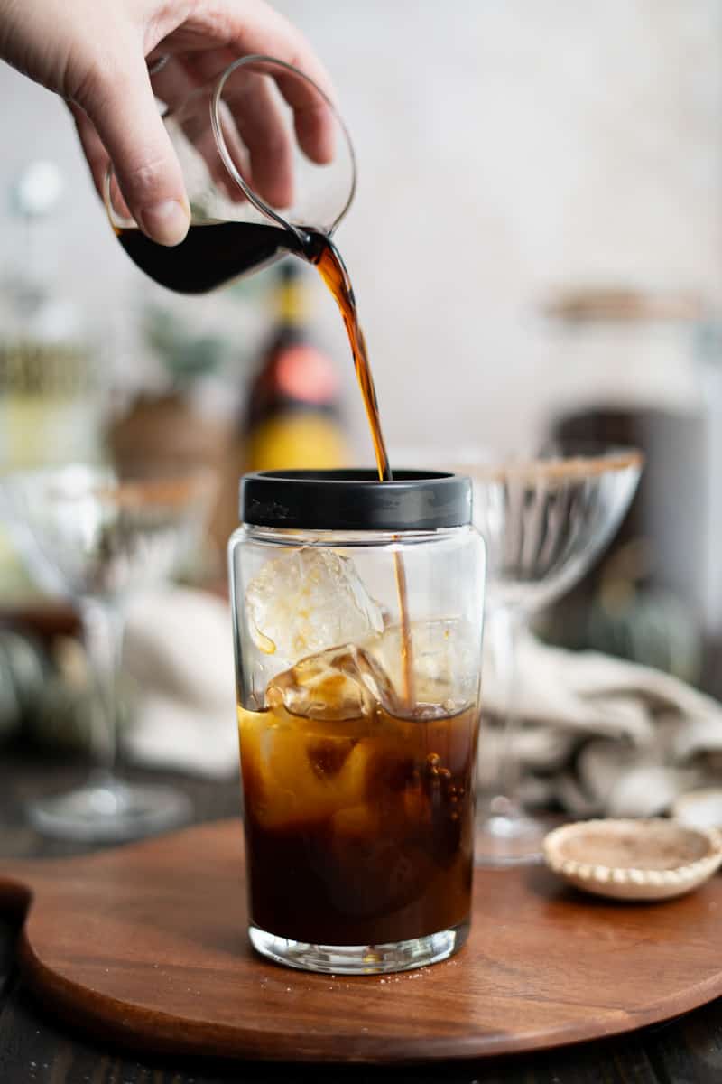 Layering Kahlua liqueur into a cocktail shaker that already has espresso, vodka, and ice.