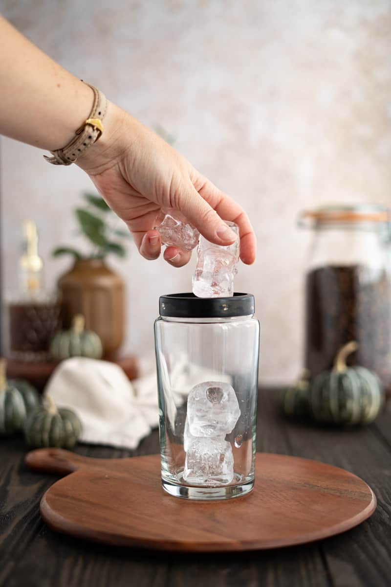 A hand from out of frame puts ice into a cocktail shaker.