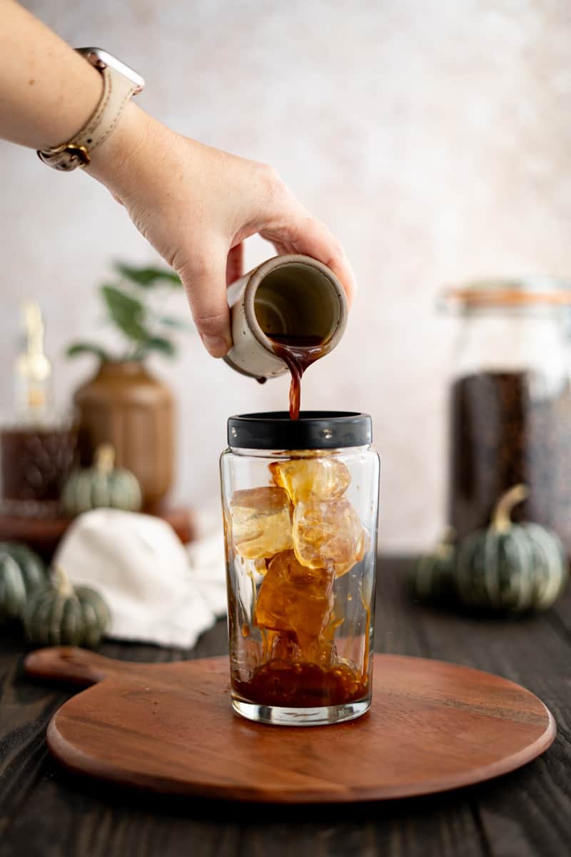 Pouring slightly cooled espresso into a cocktail shaker filled with ice cubes.