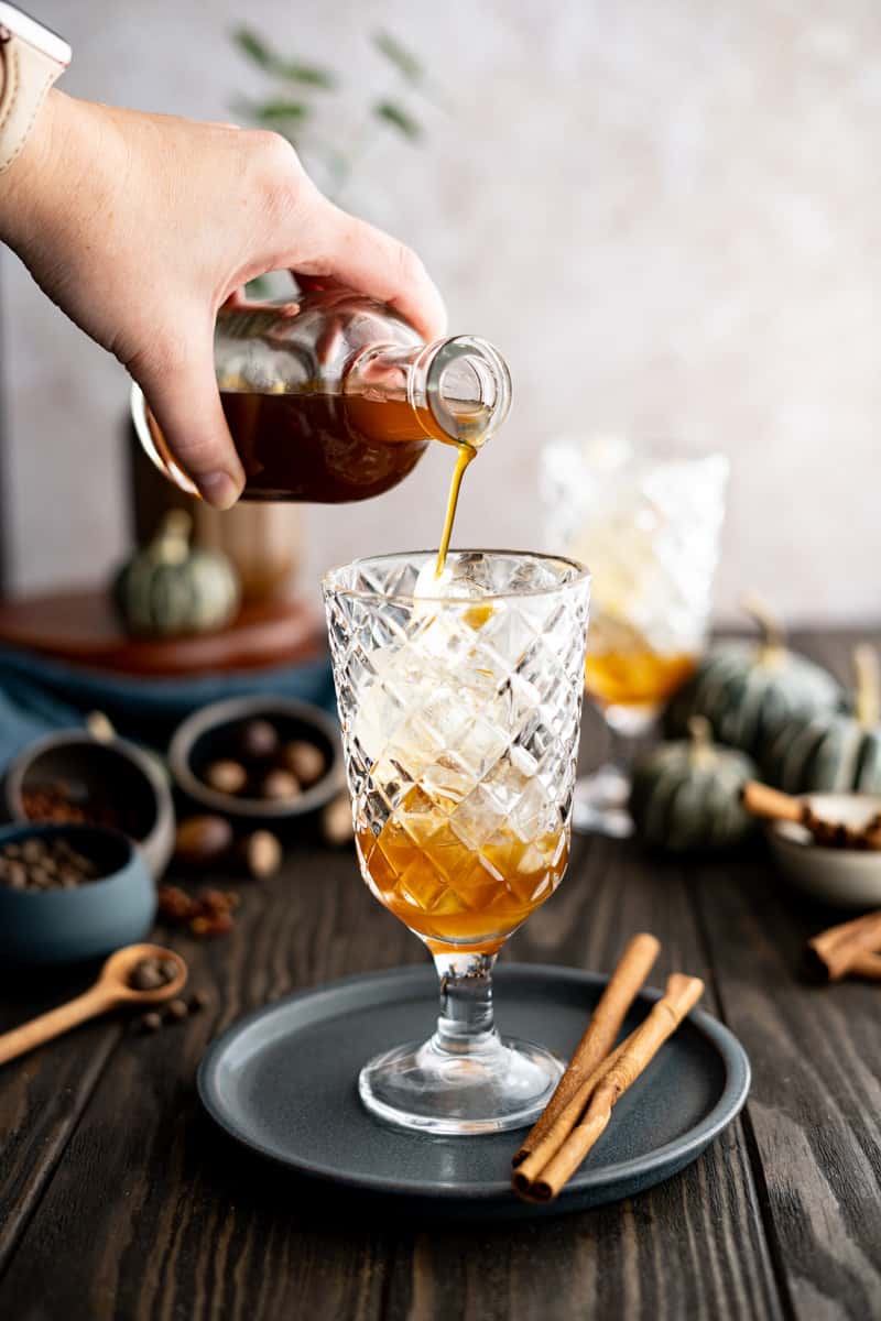 A hand from out of frame pours pumpkin spice simple syrup into a glass.