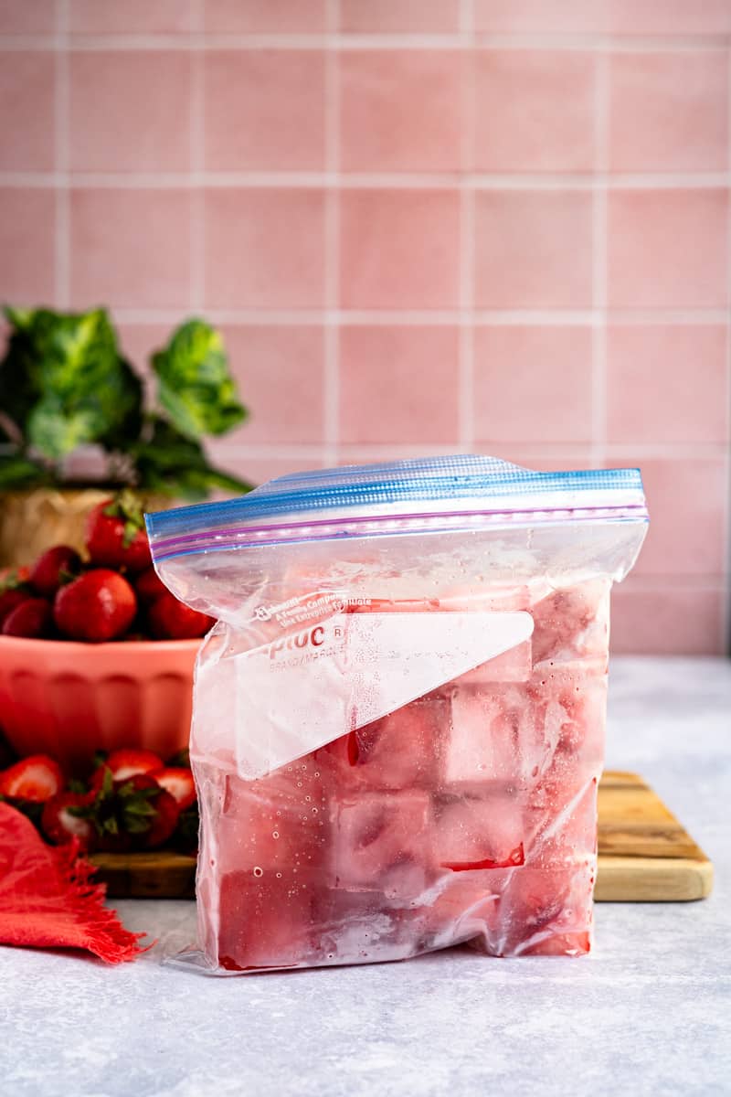 A zip-top storage bag is filled with strawberry ice cubes and ready to be placed in the freezer.