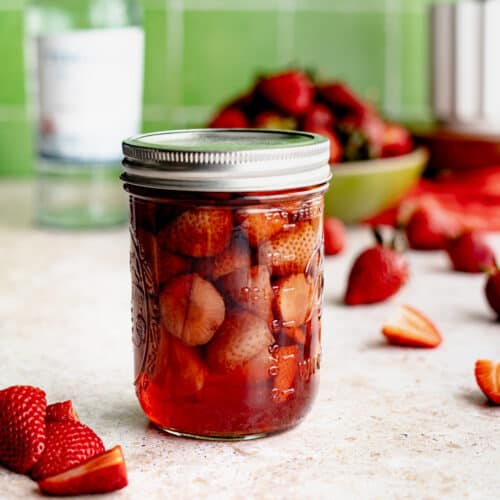 Feature image of strawberry infused tequila. A mason jar filled with strawberries infusing tequila.