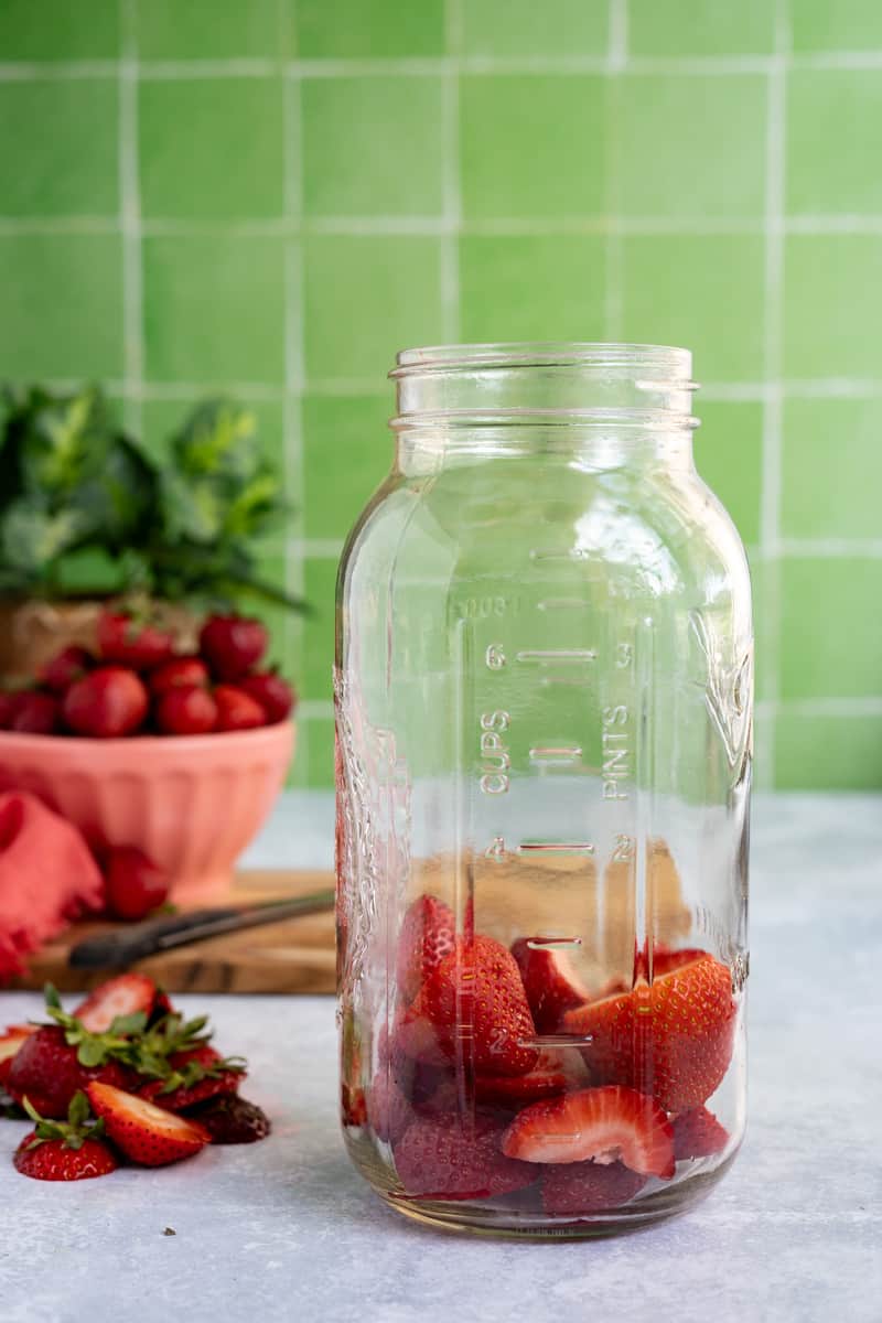 sliced strawberries are placed in a large glass mason jar.