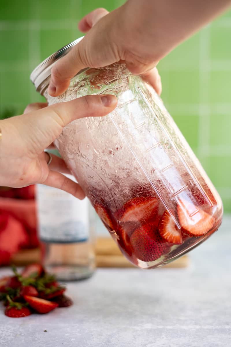 Shaking a jar of tequila and strawberries to give it help infusing.