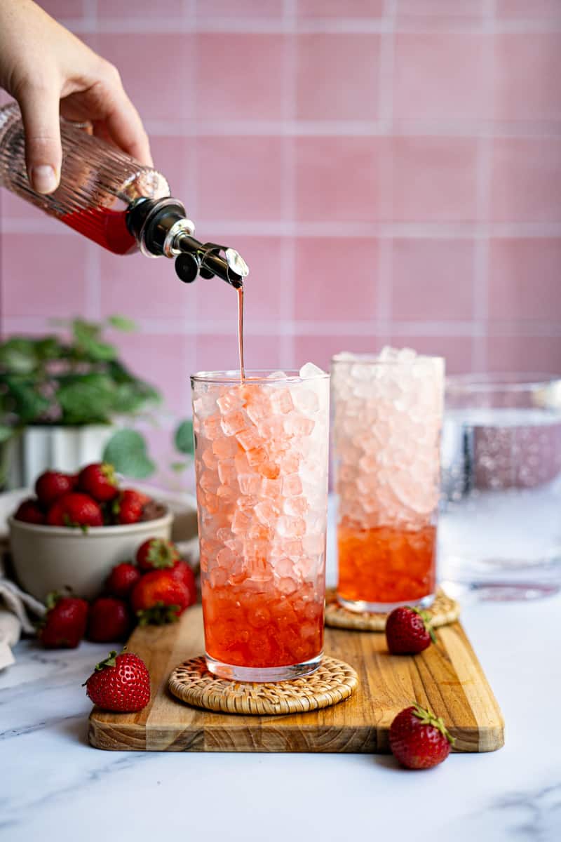 Step 2 of making strawberry Italian soda: Pour 1 ounce of strawberry syrup into the glass.