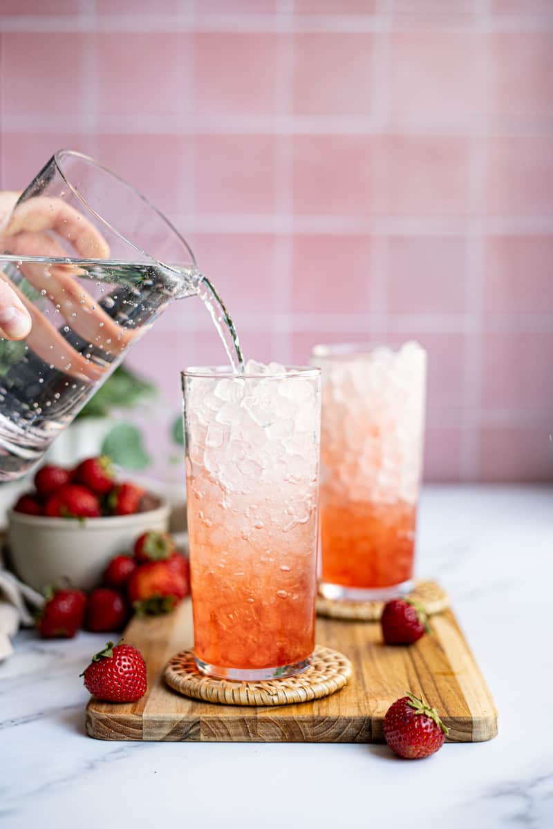 Step 3 of making strawberry Italian soda: Add soda water to the glass, filling ¾ full.
