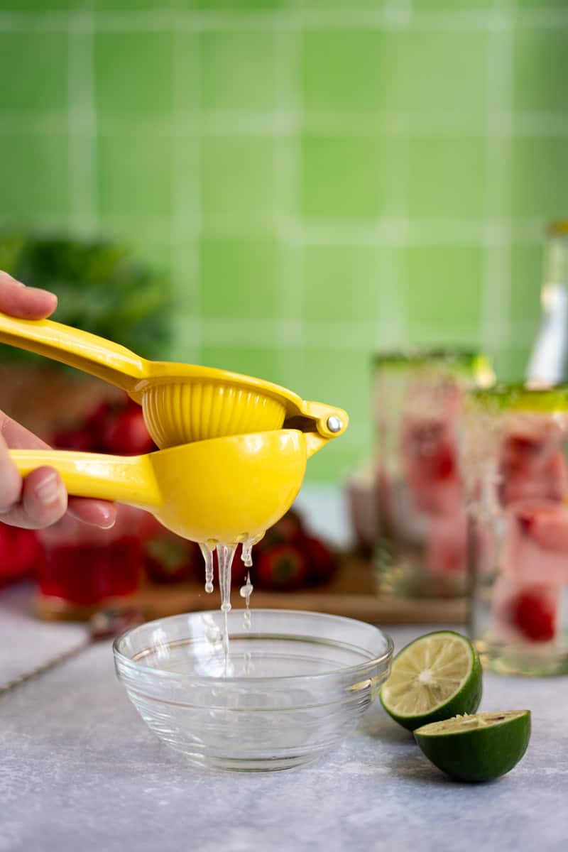 A hand from out of frame juices limes using a citrus squeezer.