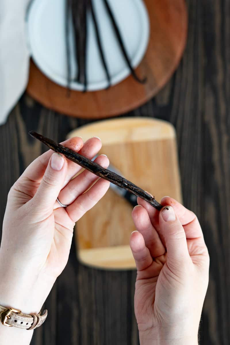 Hands show off a vanilla bean that has been sliced down the middle and pryed open.