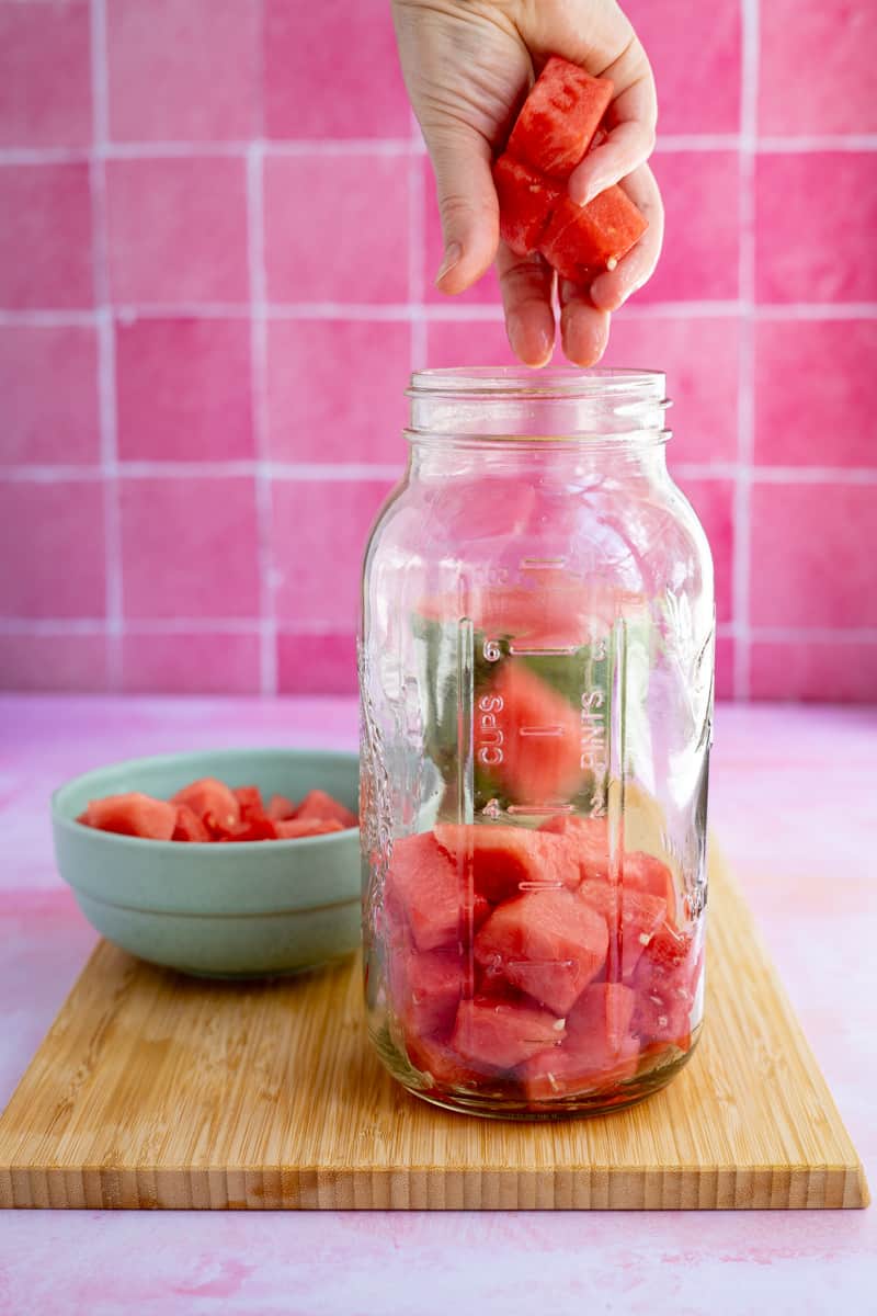 Filling a large 64 ounce jar with cubed watermelon to infuse it with tequila.