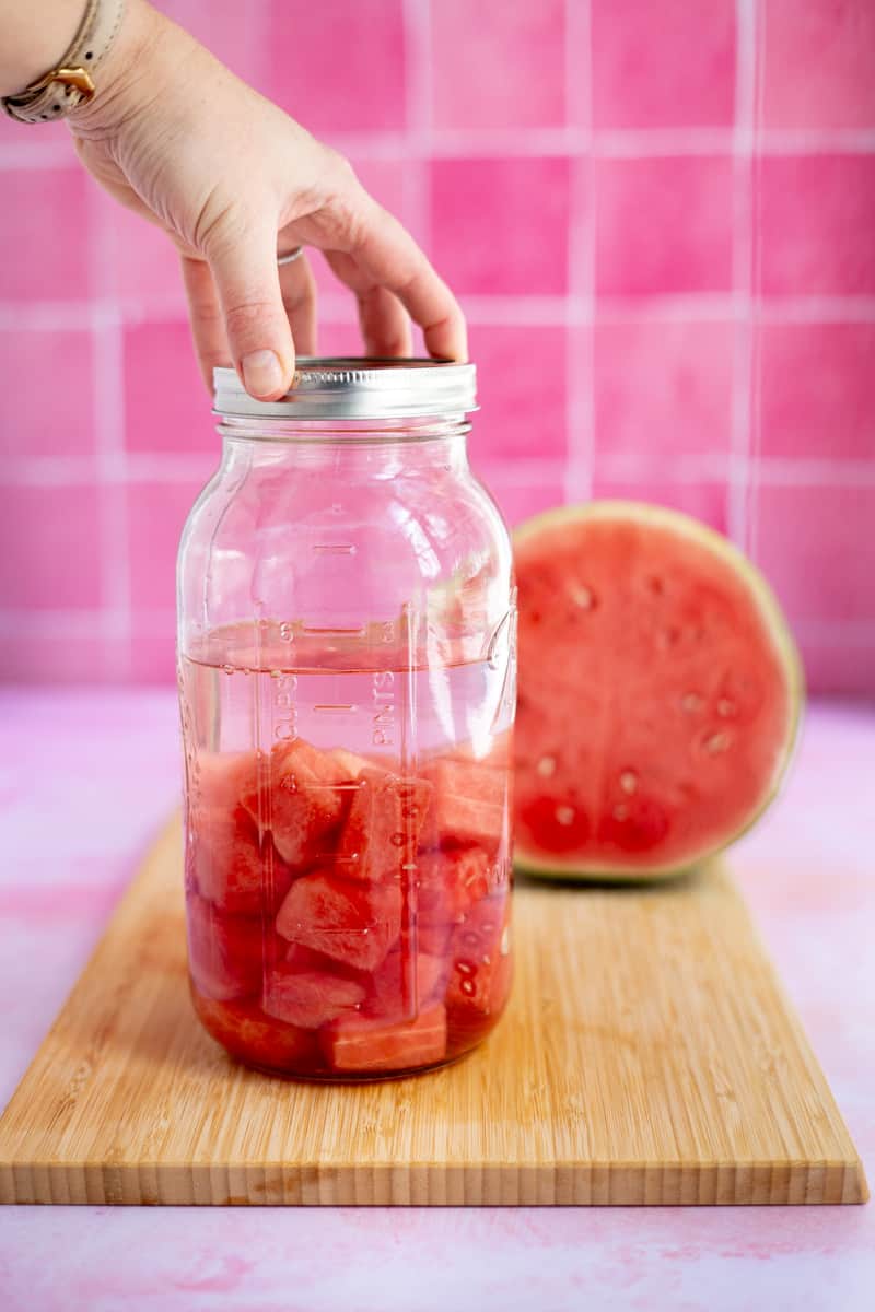 A hand from out of frame seals the jar of watermelon.