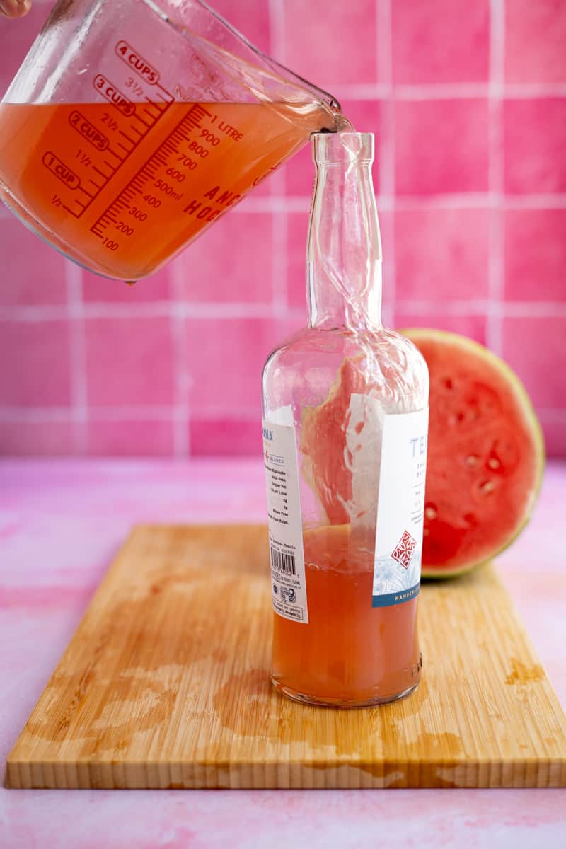 Refilling the empty bottle of tequila with the newly made watermelon infused tequila to store in the fridge.