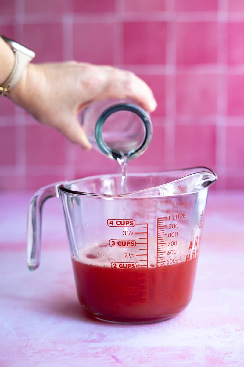 Pouring cooled simple syrup into watermelon juice to make watermelon simple syrup.