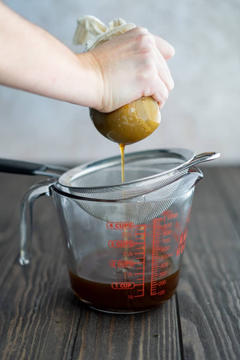 A hand squeezes cheesecloth full of pumpkin purée and spices to extract as much simple syrup as possible.
