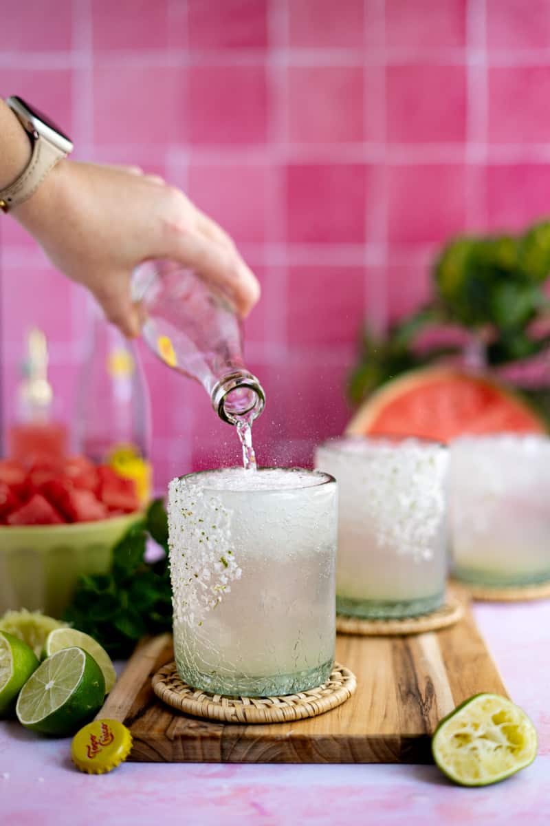 Pouring Topo Chico into a cocktail glass to finish making watermelon ranch water.