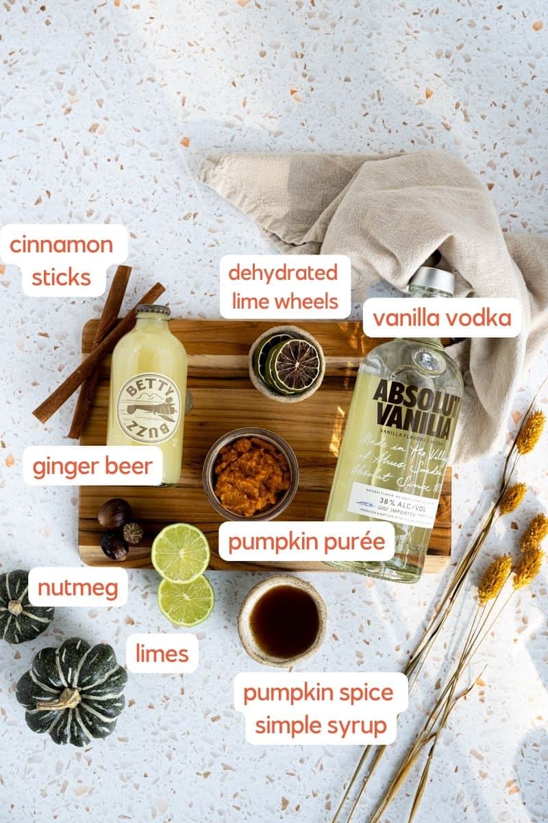 ingredients used to make a pumpkin spice mule sit on a wooden cutting board on a countertop. 