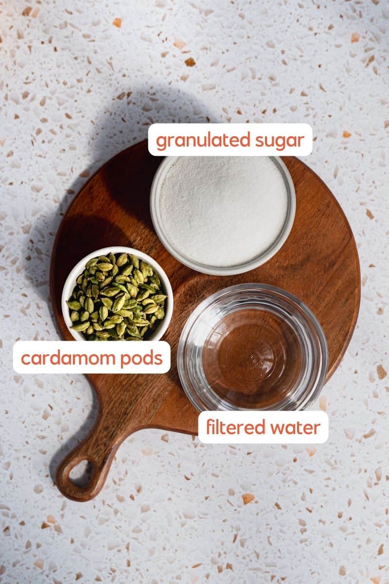 The ingredients used to make cardamom simple syrup sit on a round wooden cutting board.