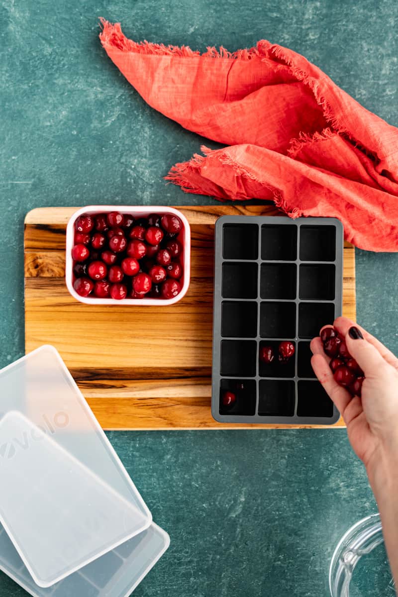 Filling an ice cube tray with cranberries.