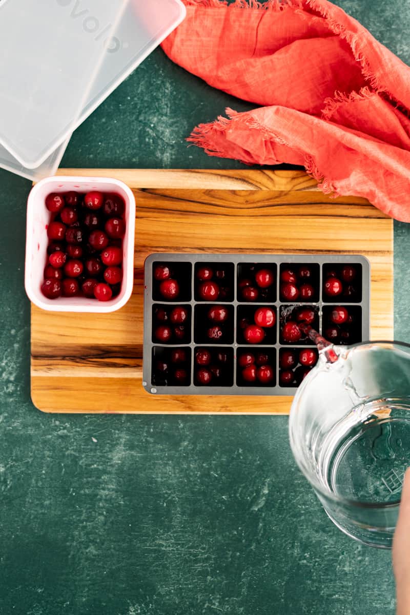 Pouring water into an ice cube tray filled with cranberries.