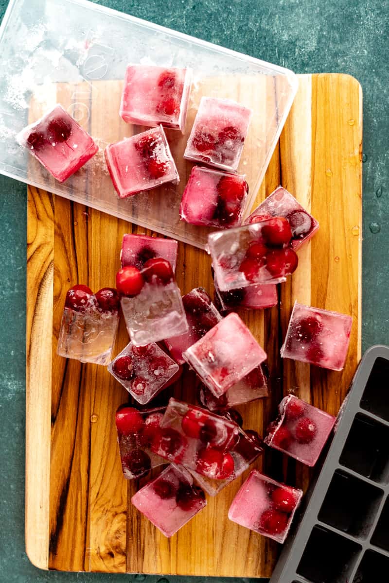 Cranberry ice cubes are scattered on a cutting board.