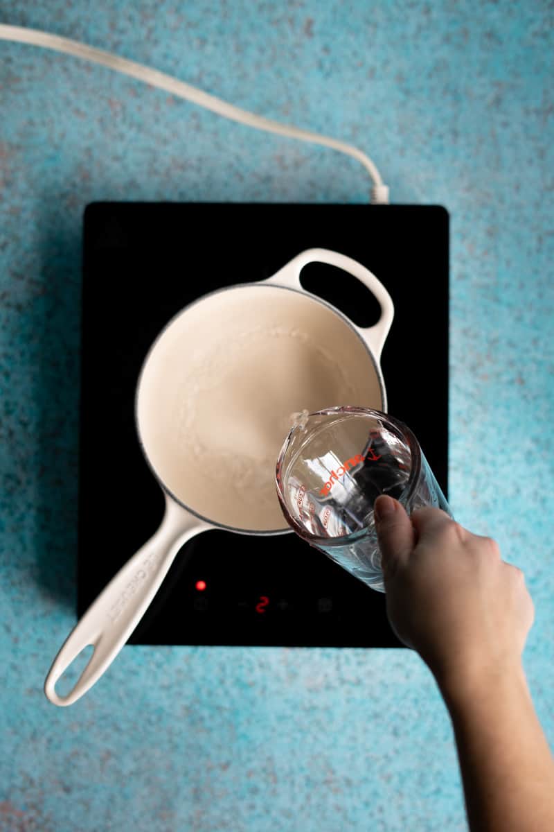 Water is being poured into a small saucepan on a heating plate.