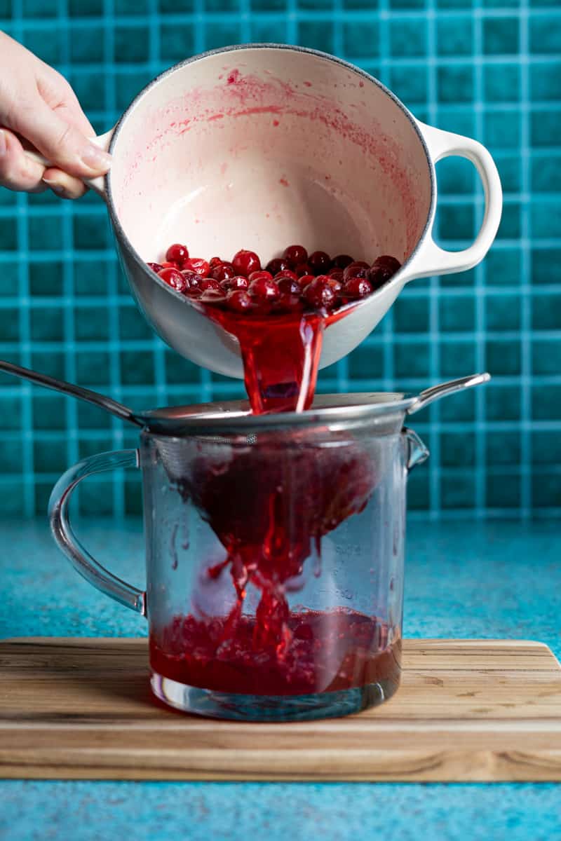 Straining the cranberry simple syrup through a fine mesh sieve into a measuring cup to cool.