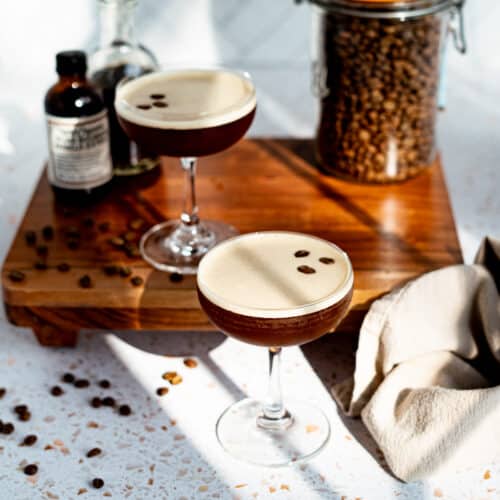 Feature image for an espresso martini mocktail. Two glasses of virgin espresso martinis sit on a countertop next to the ingredients used to make them.