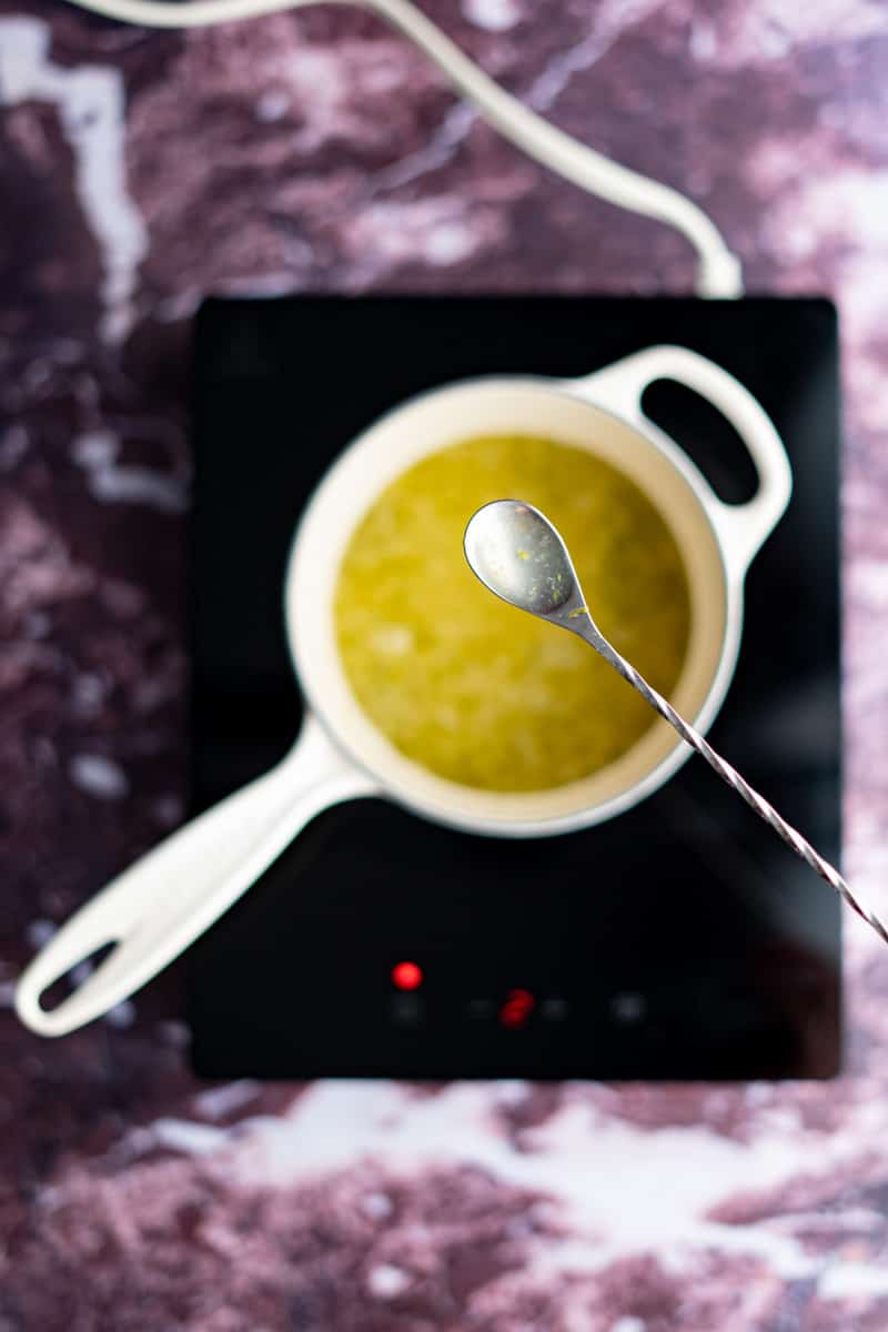 A cocktail spoon holds up a small amount of key lime simple syrup with the intention to taste it for flavor.