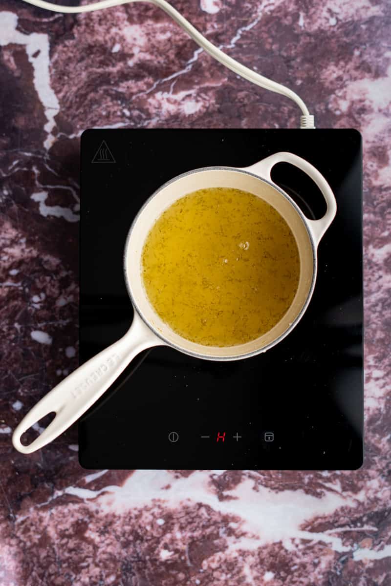 A saucepan with key ilme simple syrup sits on a saucepan cooling. The syrup has deepened in color.