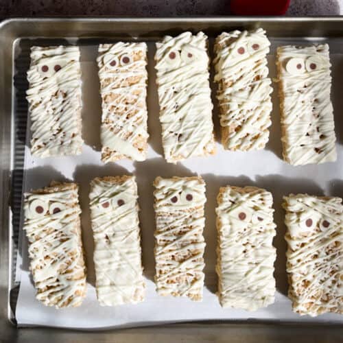 Feature image for mummy rice krispie treat recipe. Mummy rice krispie treats sit on a baking sheet ready to be served or stored.