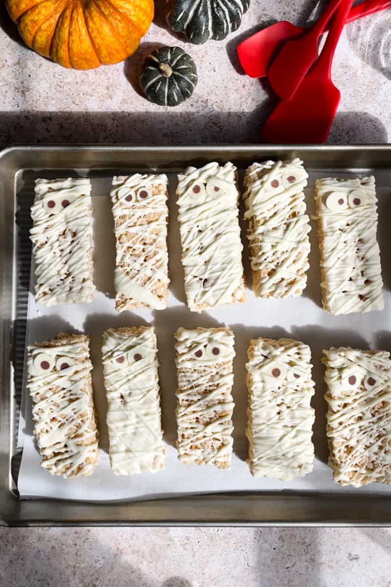 Feature image for mummy rice krispie treat recipe. Mummy rice krispie treats sit on a baking sheet ready to be served or stored.