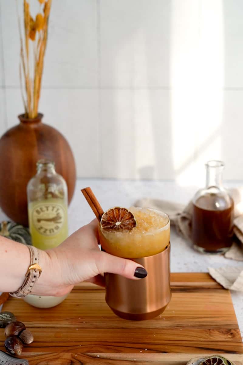 A hand from out of frame grabs a pumpkin spice mule from a countertop.