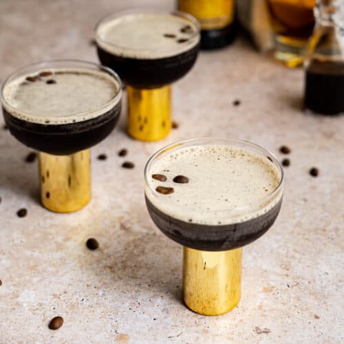 Feature image for a rum espresso martini. Three rum espresso martinis sit on a countertop that is scattered with espresso beans.