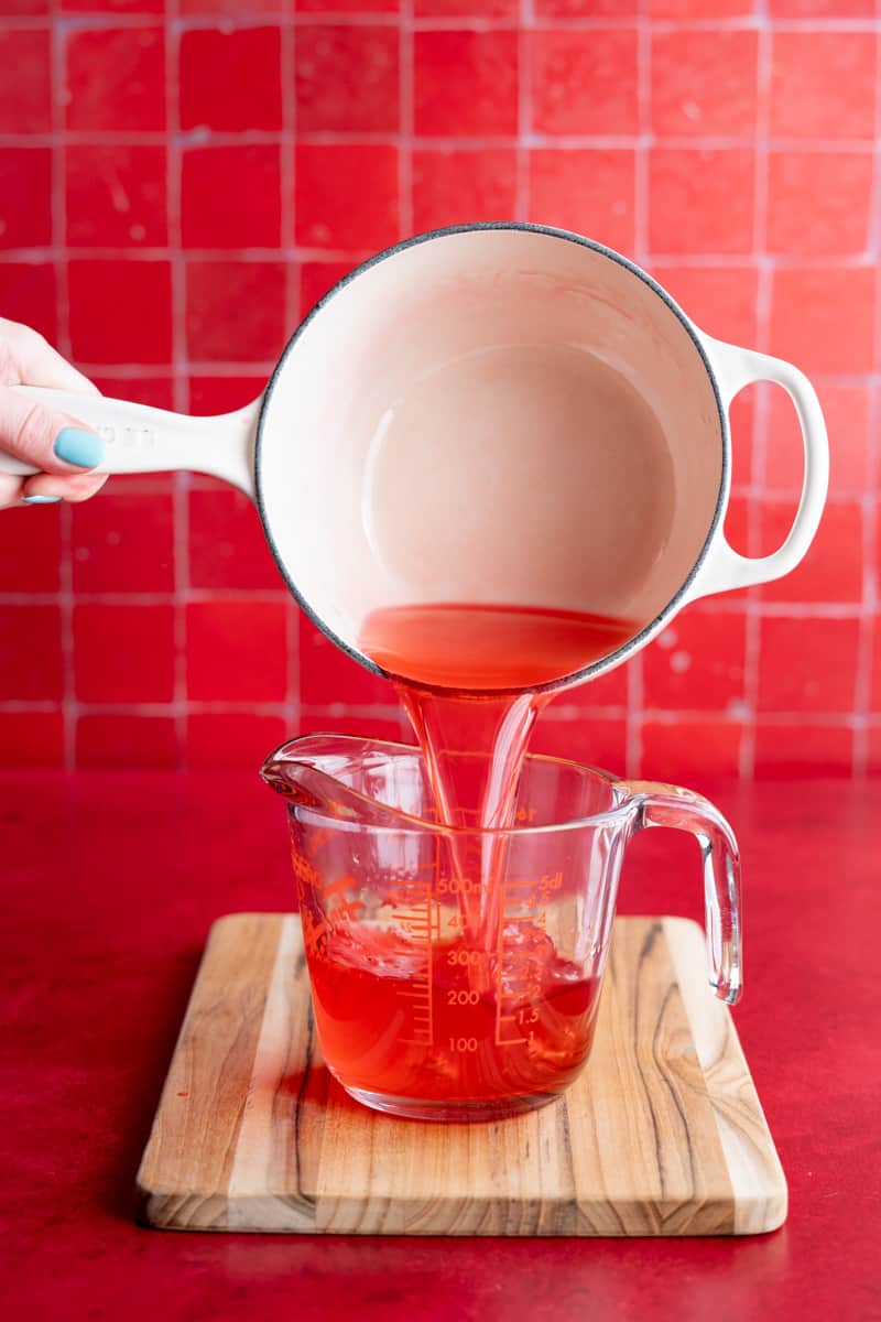 Pouring cooled candy cane syrup from the saucepan to a measuring glass.
