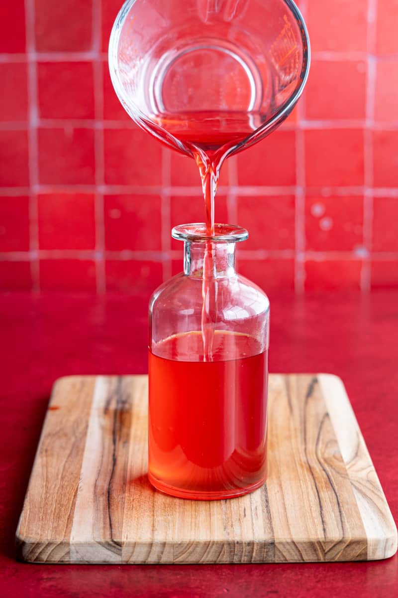 Pouring candy cane syrup into a storage bottle for storage.