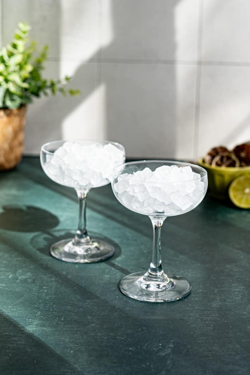 Chilling two coupe glasses by filling them with ice.