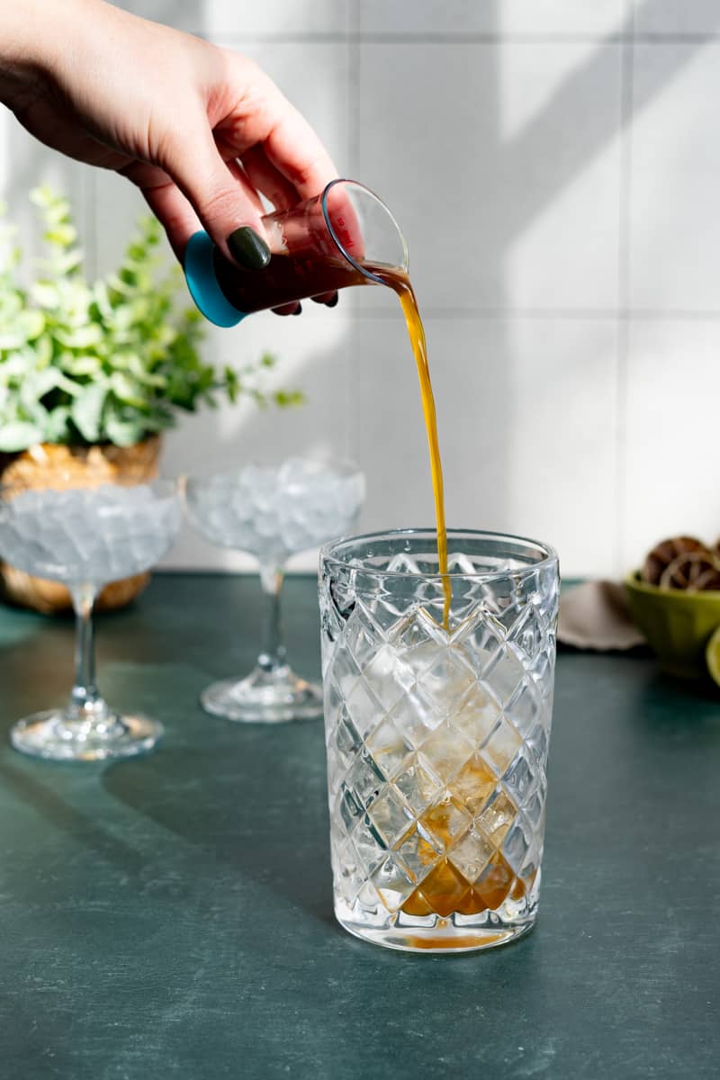 Adding demerara simple syrup to a cocktail shaker filled with ice.