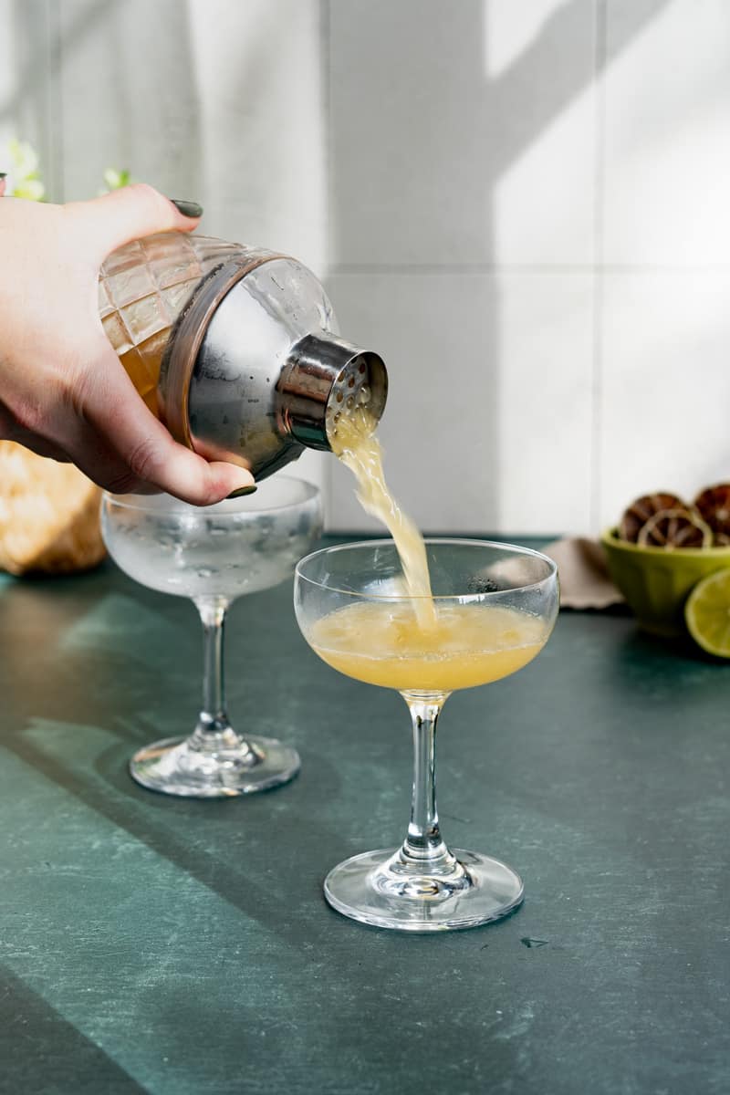 A hand from our of frame pours a Cuban daiquiri into a cocktail coupe.