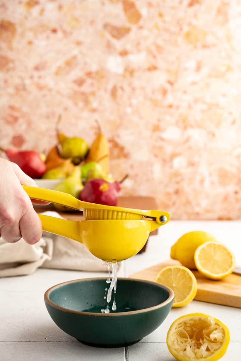 A hand from out of frame is juicing lemons in a handheld citrus press.