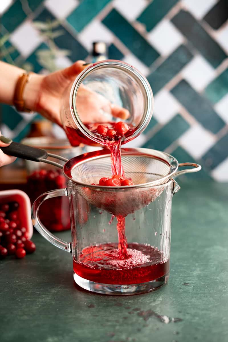 Pouring the cranberry gin through a fine mesh sieve to strain the cranberries out of the mix.