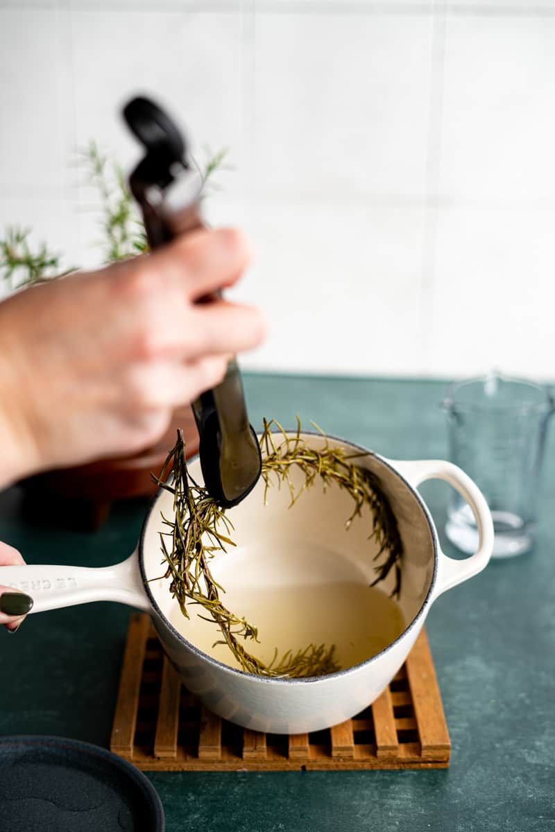 Removing the infused rosemary from the saucepan.
