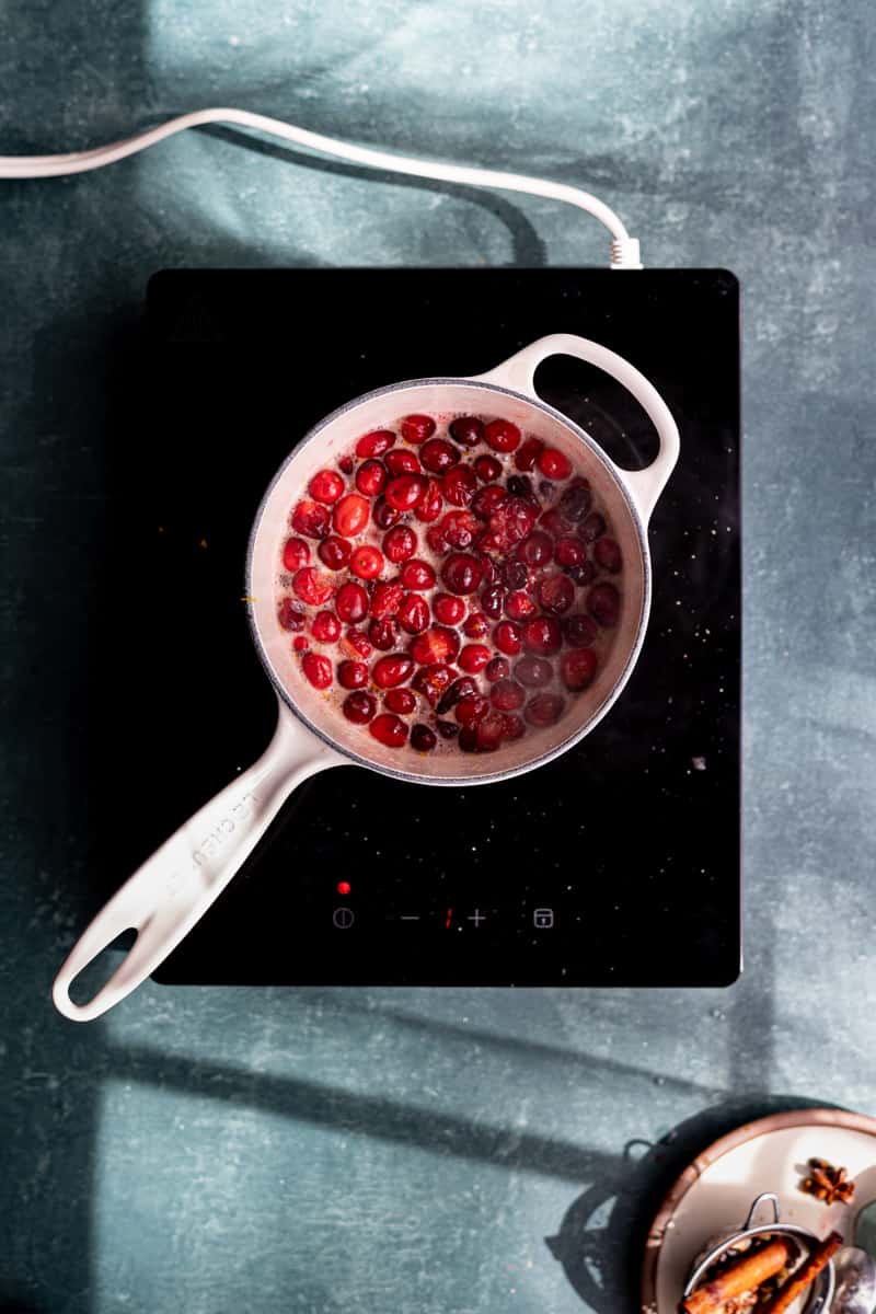 A saucepan of simmered cranberries cools on a hotplate.