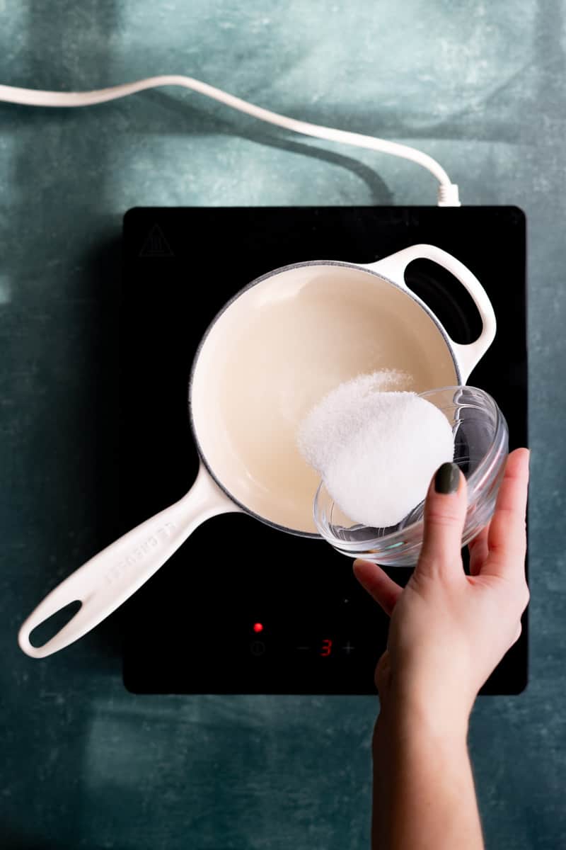 Pouring sugar into a saucepan to make a simple syrup.
