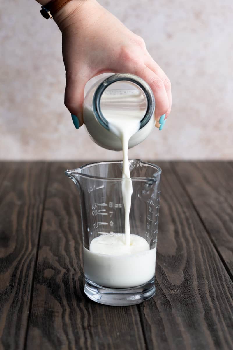 A hand from out of frame pours milk into a measuring glass.