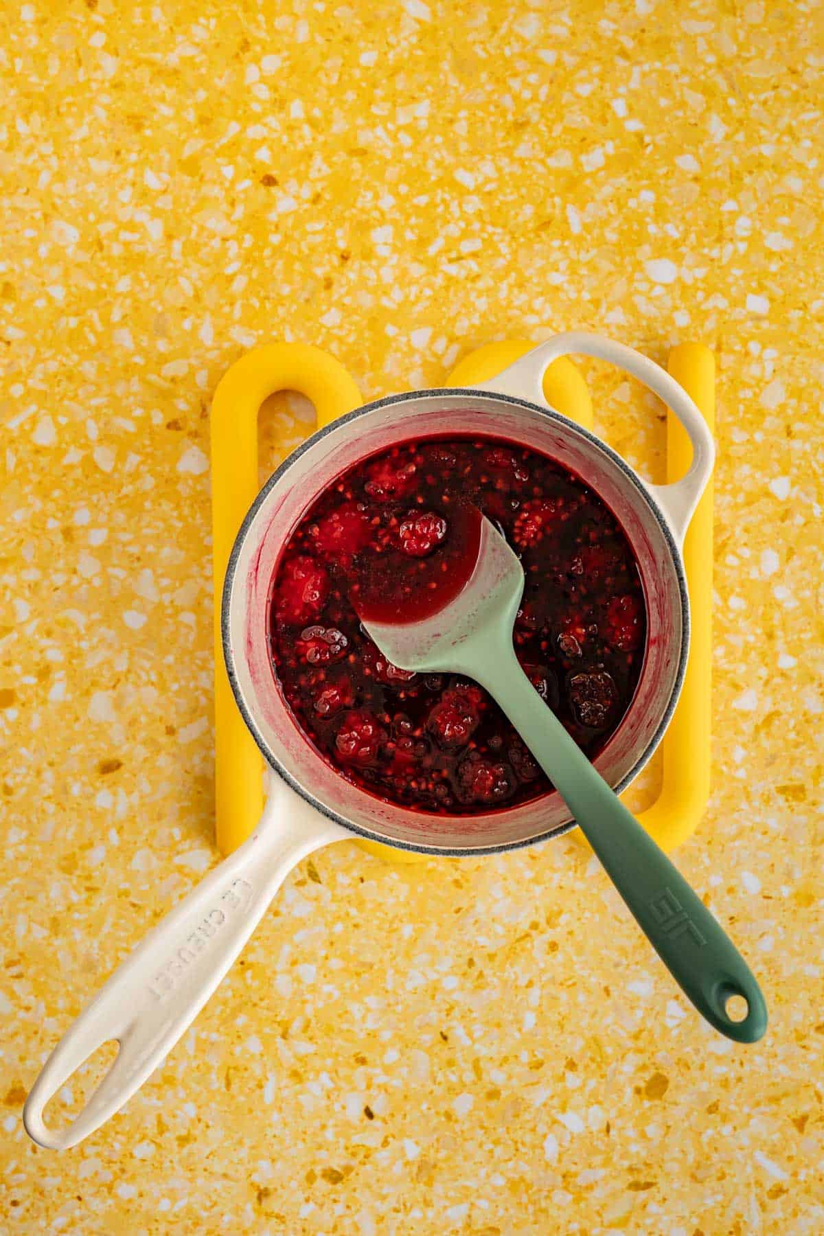 A saucepan of infused blackberry simple syrup is sitting on a yellow terrazzo countertop.