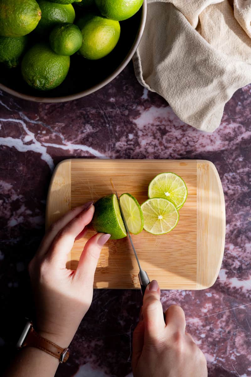 Hands from out of frame are slicing limes to dehydrate.