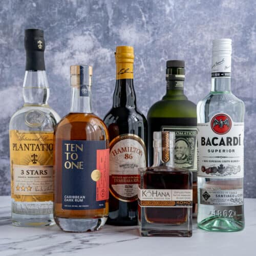 A collection of different types of rum bottles sit on a countertop. The bottles range in size and type of rum.