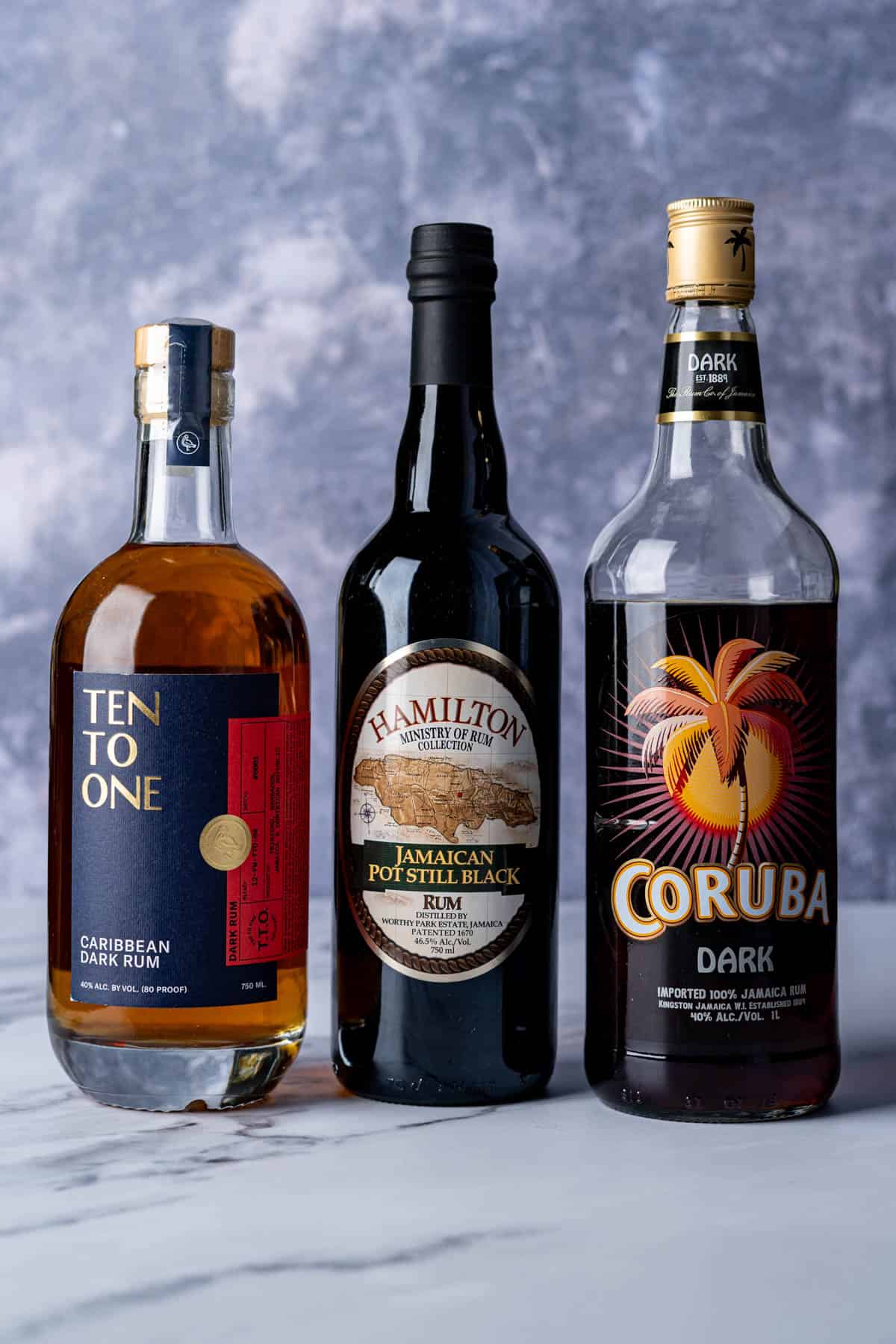 Three bottles of dark rum, also known as black rum, sit on a countertop.